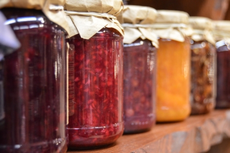 Canning jars lined up on a wooden shelf filled with various Jellies and Jams