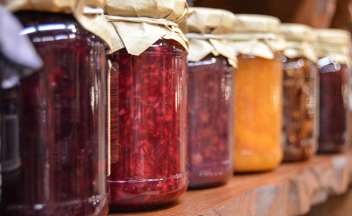 Canning jars lined up on a wooden shelf filled with various Jellies and Jams